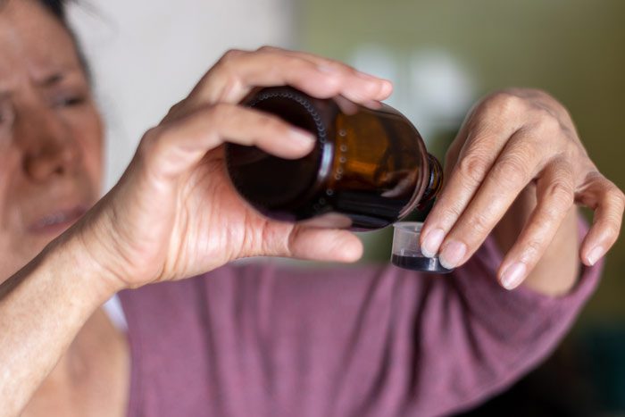 codeine opiate addiction, woman pouring cough medicine into a measuring cup - codeine