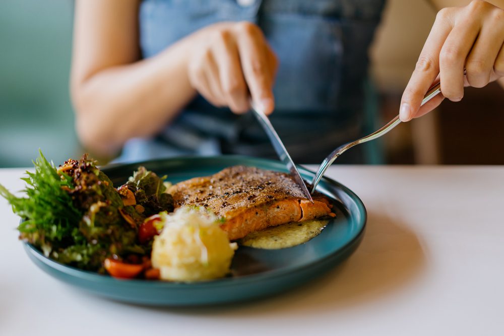 A woman eating a healthy meal - salmon and veggies