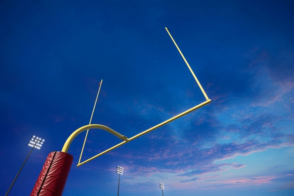 Low-angle view of a football goalpost under stadium lights at dusk, with a dramatic sky in the background, symbolizing goals or shifting expectations.