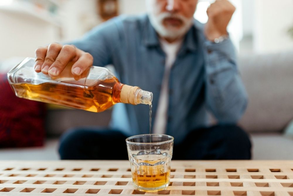 Close-up of a man pouring whiskey into a glass while sitting at a table.