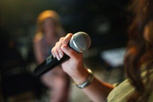 A hand holding a microphone with a blurred figure in the background.